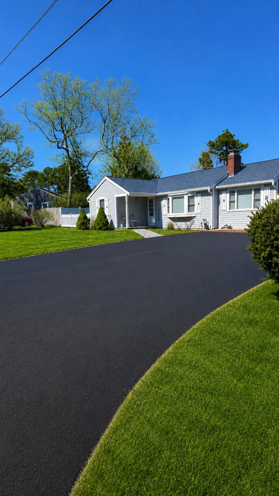 Finished curved black asphalt driveway beside a Cape Cod home